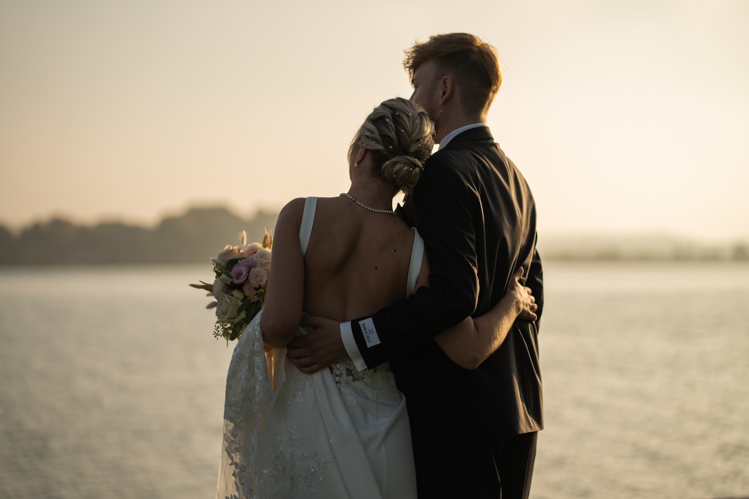 Ein Paar steht eng umschlungen am Wasser bei Sonnenuntergang – emotionales Bild für den Kundenstimmen-Bereich.