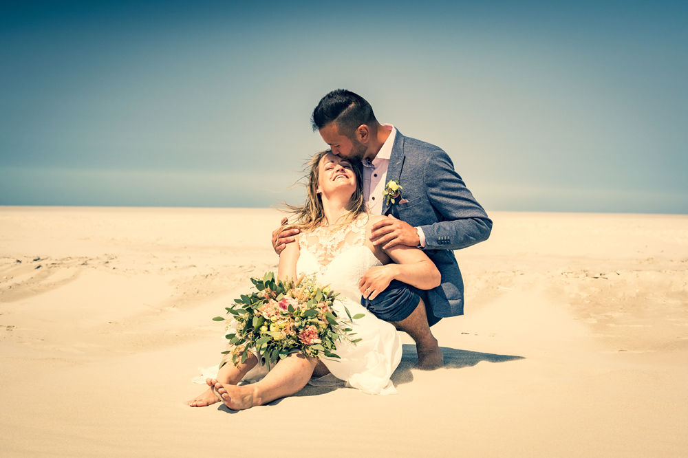 Ein Paar sitzt liebevoll am Strand – stimmungsvolles Bild für die Kundenstimmen der Hochzeitsplanung.