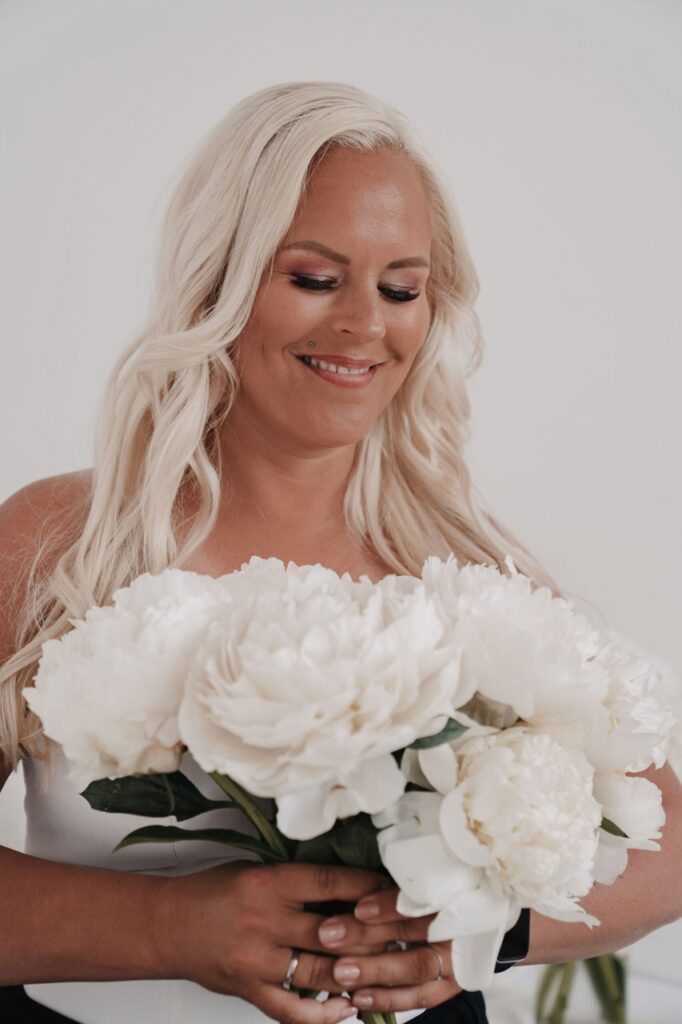 Svenja Feddersen, Hochzeitsplanerin in Hamburg und Schleswig-Holstein, hält einen weißen Blumenstrauß und lächelt im hellen Studio.