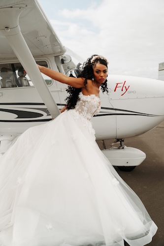 Braut in einem eleganten Hochzeitskleid posiert vor einem Flugzeug und schafft einen exklusiven, modernen Hochzeitslook.
