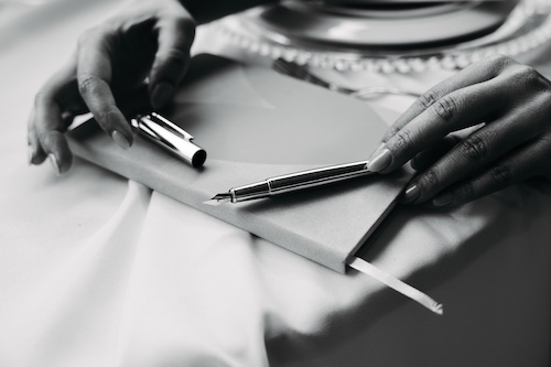 Detailaufnahme von Händen mit offenem Notizbuch und Füllfederhalter – Symbol für den strukturierten Ablaufplan einer Hochzeit.