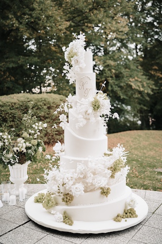Mehrstöckige weiße Hochzeitstorte mit floralen Verzierungen im Garten.